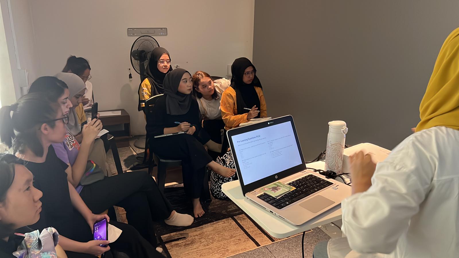 Trainees taking notes during a classroom session with pre-learning questions on screen